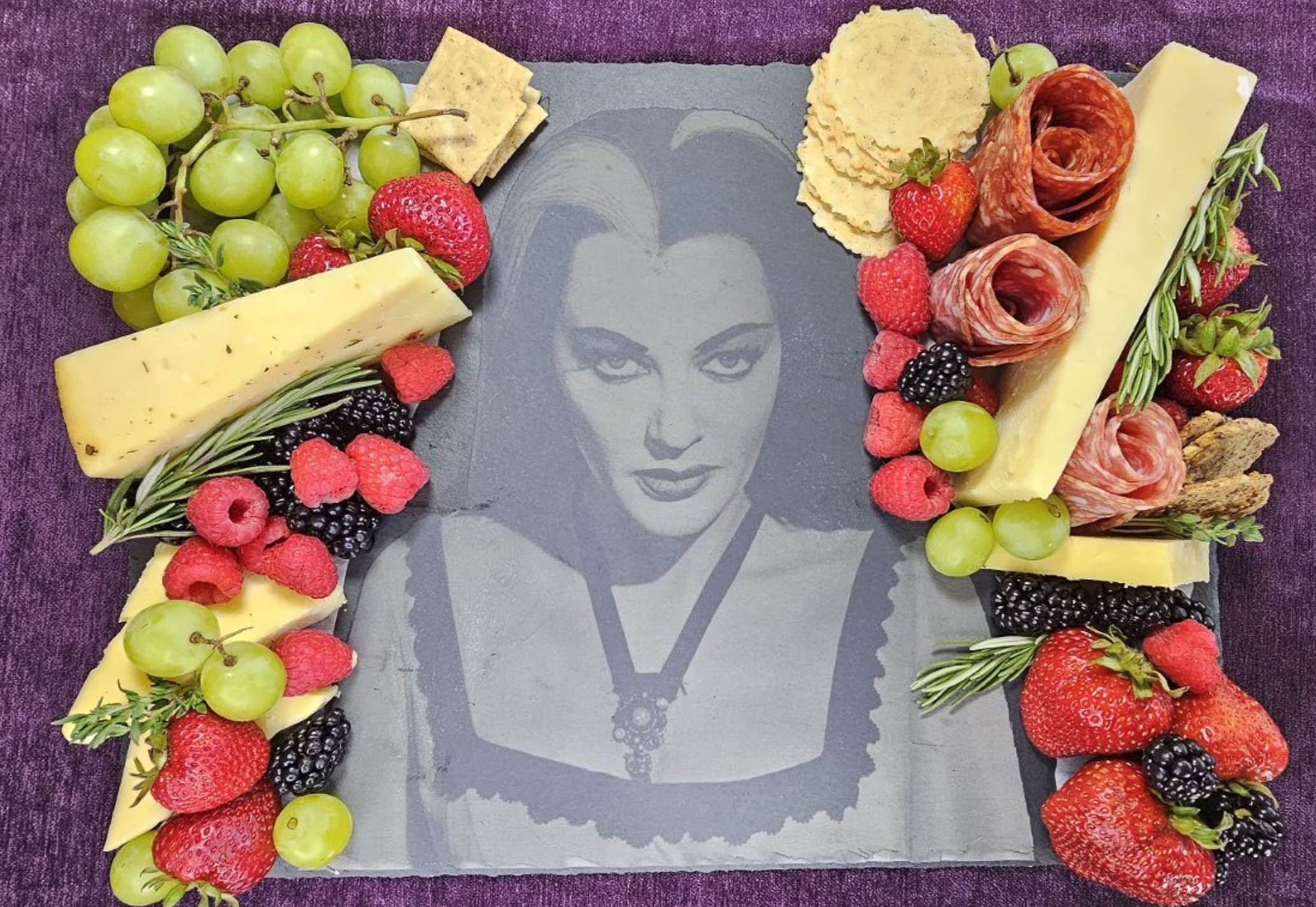 Lily Munster collectible displayed as centerpiece of elegant charcuterie board with fresh fruits, cheeses, and gourmet meats